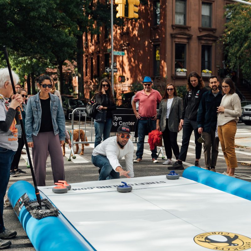 A large inflatable curling surface on a city street with various people playing.